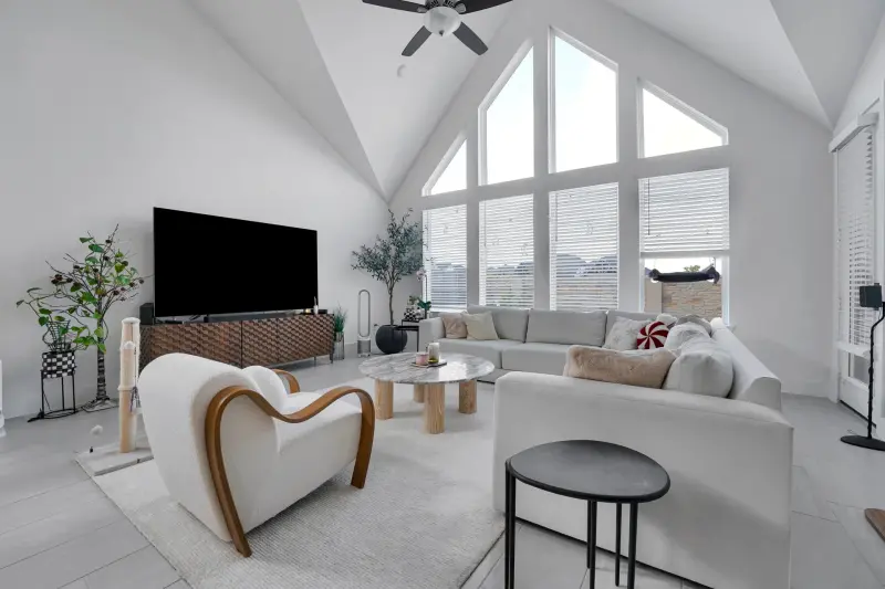 Sun-filled vaulted living room with cathedral windows and a sculptural boucle chair; well staged. — Houston real estate photography