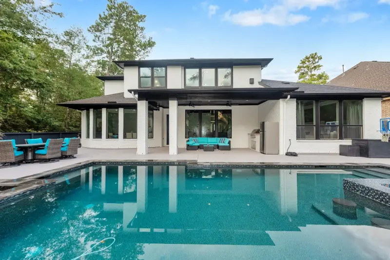 Sleek modern home mirrored in a large rectangular pool under tall pines. — Houston real estate photography