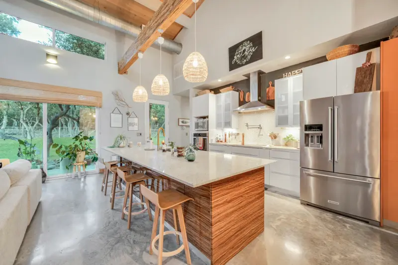 Magazine-grade kitchen with vaulted beam ceiling, rattan pendants, waterfall island and styled decor; airy and luminous. — Austin–San Antonio corridor real estate photography