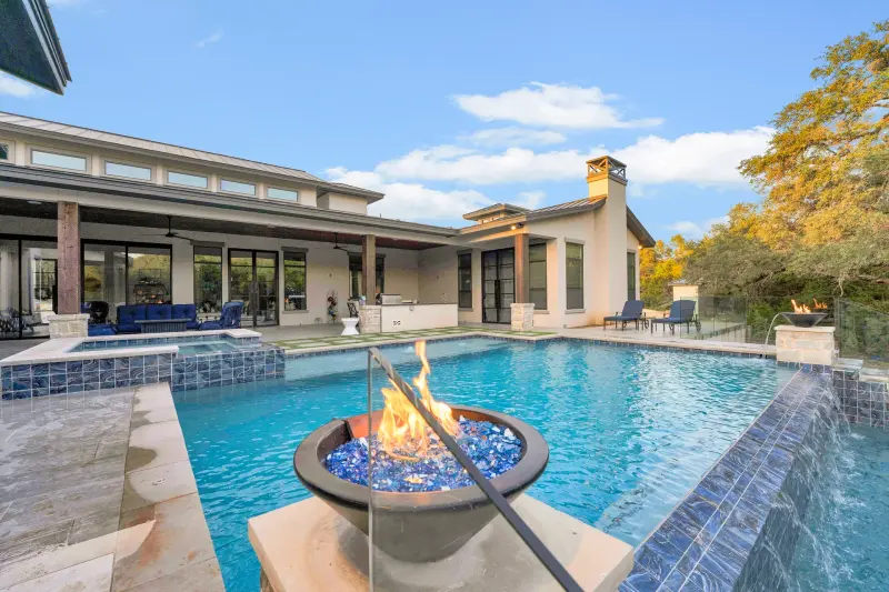 Hero shot: luxury pool with lit fire bowl in foreground, modern home, blue sky reflections. High wow-factor. — San Antonio real estate photography