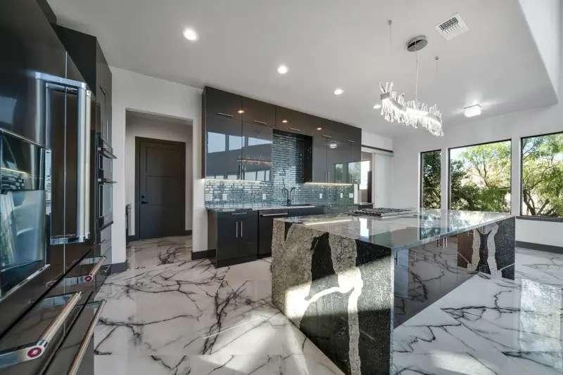 Marble waterfall island kitchen with statement chandelier and walls of glass — Austin real estate photography