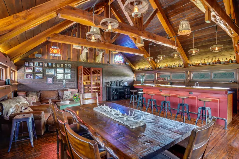 Great room dining beneath exposed heavy-timber trusses with a wall of ranch views — Austin–San Antonio corridor real estate photography